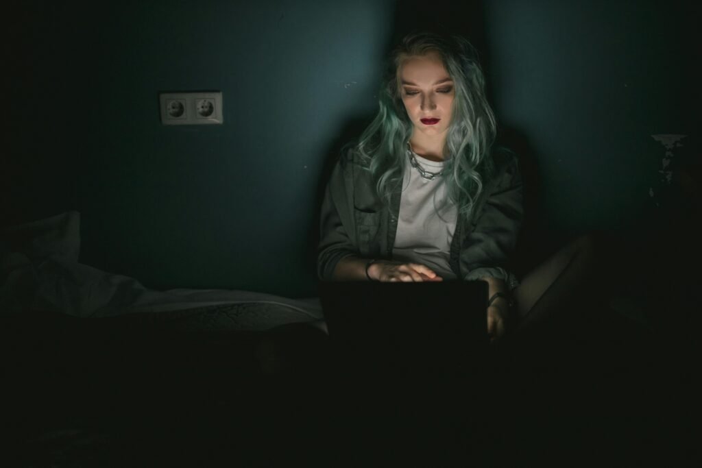 Jovem com expressão séria utiliza laptop em ambiente escuro, representando uso de aplicativo digital para prevenção do suicídio e apoio em saúde mental.