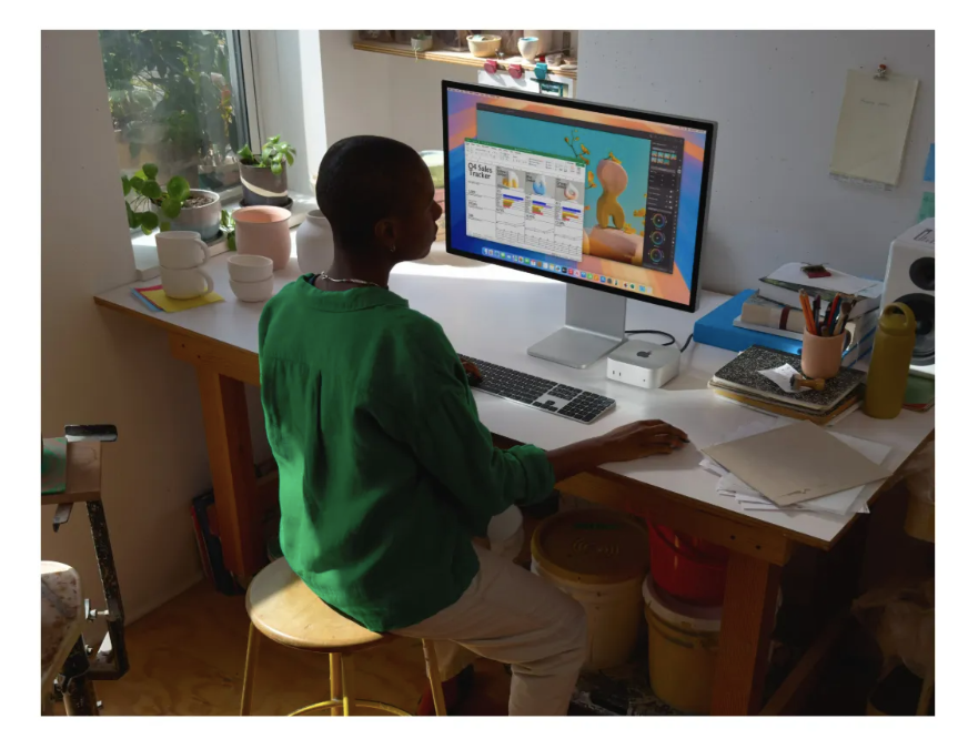 Usuário trabalhando em monitor com Mac mini M4 na mesa, demonstrando uso profissional do mini PC Apple para produtividade e criação